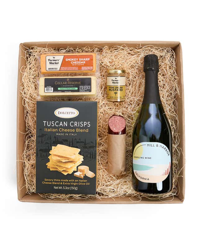 A gift box with Tuscan crisps, salami, cheeses, mustard, and a bottle of Hill &amp; Harbor sparkling wine. Surrounding the box are plates with cheese, salami, mustard, and two glasses of sparkling wine.