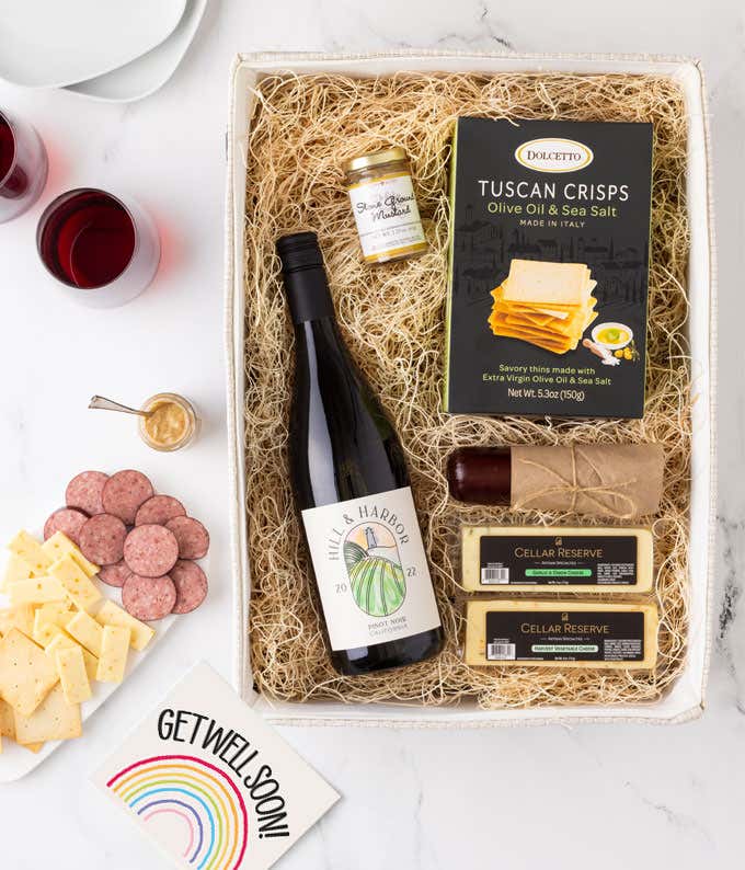 A gift box with a bottle of California Pinot Noir, two types of cheese, crackers, stone-ground mustard, a summer sausage and a Get Well Soon message card.