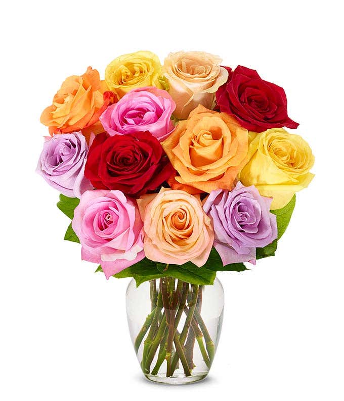 A bouquet of multicolored roses in a clear vase, featuring red, pink, orange, yellow, peach, and lavender blooms, arranged with green leaves for a vibrant and cheerful display.