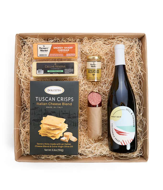 A gift box with a bottle of California Pinot Noir, two types of cheese, crackers, stone-ground mustard, and a summer sausage.