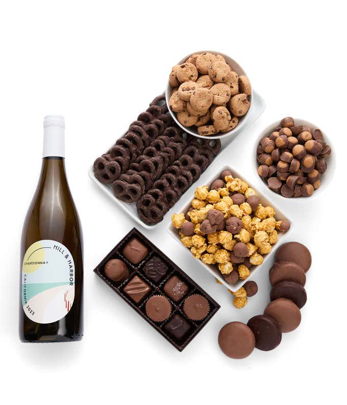 A gift set featuring a bottle of Hill & Harbor White Wine alongside chocolate-covered pretzels, mini cookies, caramel popcorn, chocolate-covered almonds, and 6 chocolate-covered Oreos. Includes a box of assorted chocolates for a luxurious touch.