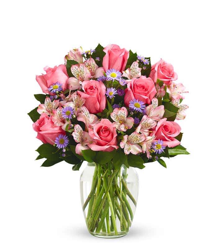 A bouquet of pink roses, white alstroemeria, and lavender aster in a glass vase 