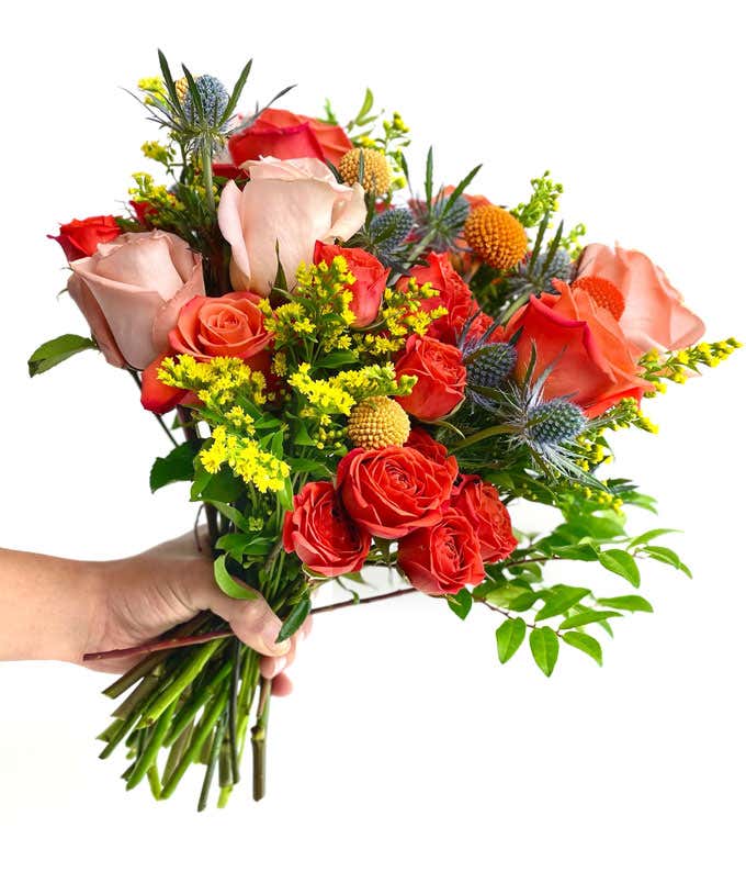  A vibrant floral arrangement featuring coral roses, peach roses, coral mini roses, yellow solidago, yellow craspedia, orange craspedia, and blue eryngium, complemented by a personal card message and optionally presented in a vase.