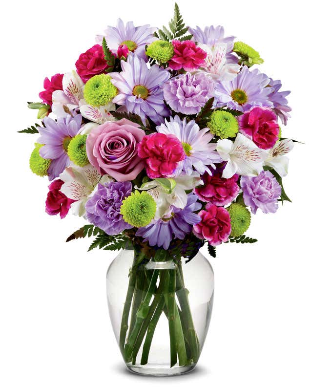 A bouquet featuring lavender daisies, lavender roses, hot pink mini carnations, lavender carnations, white alstroemeria, and green button poms, with an optional vase.