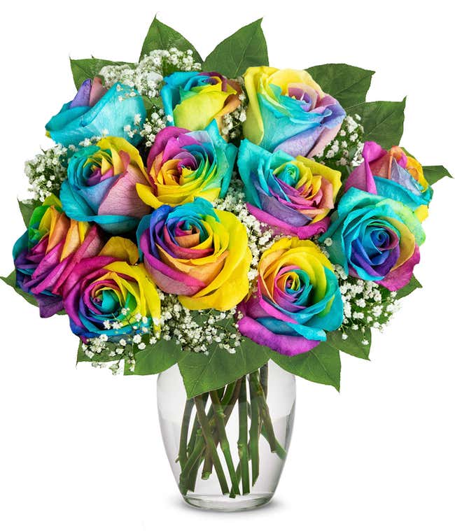 A colorful bouquet of rainbow roses in a clear glass vase, with petals in vibrant hues of blue, yellow, pink, and purple, accented by baby's breath and green leaves, creating a bright and cheerful display.