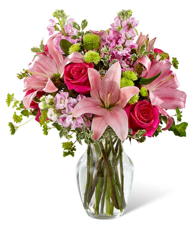 Pink lilies, roses, and gilly flowers, with fresh floral greens in a clear glass vase