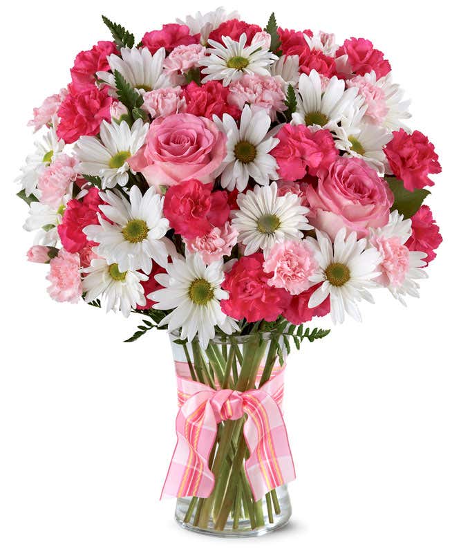 A delightful arrangement featuring hot pink spray roses, white traditional daisies, and pink mini carnations, beautifully arranged in a clear vase with a pink bow. This vibrant mix offers a cheerful and elegant display.