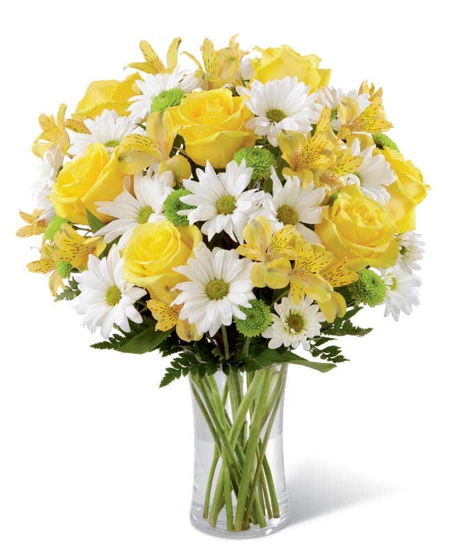 A bright floral arrangement featuring yellow roses, white daisies, yellow alstroemeria, and green poms, elegantly arranged in a glass vase. This sunny mix offers a cheerful and uplifting display.