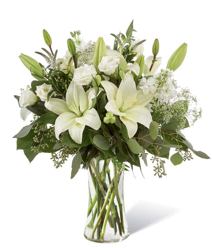 An elegant arrangement featuring white lilies, white lisianthus, white stock, Queen Anne's lace, white veronica, and eucalyptus, beautifully presented in a tall clear cylinder vase. Includes a complimentary card message for a personal touch.