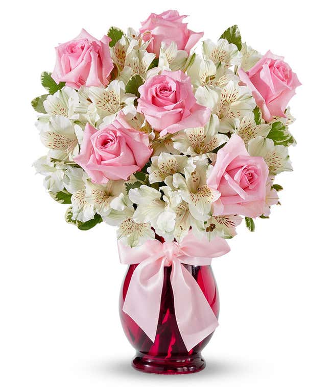 A charming arrangement featuring pink roses and white alstroemeria, beautifully presented in a pink fluted vase with a decorative ribbon. This elegant display offers a perfect blend of colors and sophistication for any occasion.