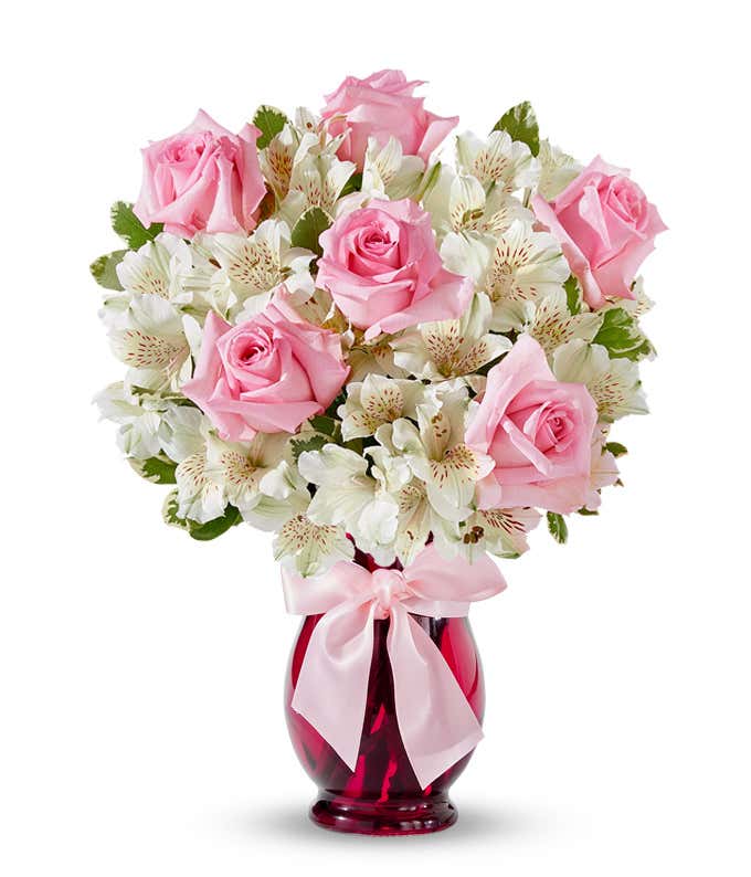 A charming arrangement featuring pink roses and white alstroemeria, beautifully presented in a pink fluted vase with a decorative ribbon. This elegant display offers a perfect blend of colors and sophistication for any occasion.