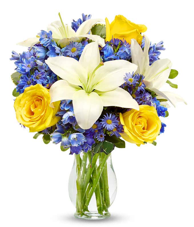 Yellow roses, blue delphinium and white lilies in a vase for Mothers Day