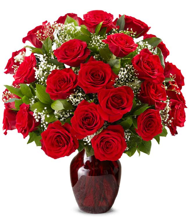 A classic arrangement of one dozen red roses, accented with baby's breath, elegantly presented in a red glass vase. This timeless display offers a romantic and sophisticated touch.