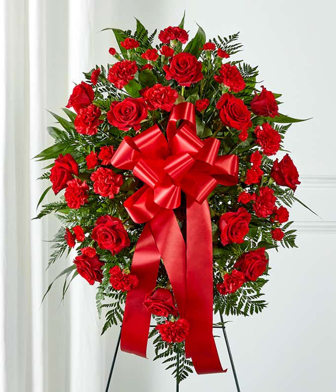 A heartfelt standing spray featuring red roses and carnations with floral greens, arranged by your local florist and hand-delivered with a decorative red bow. Measuring 21H by 32L, this arrangement is a beautiful way to show love and support during hard t