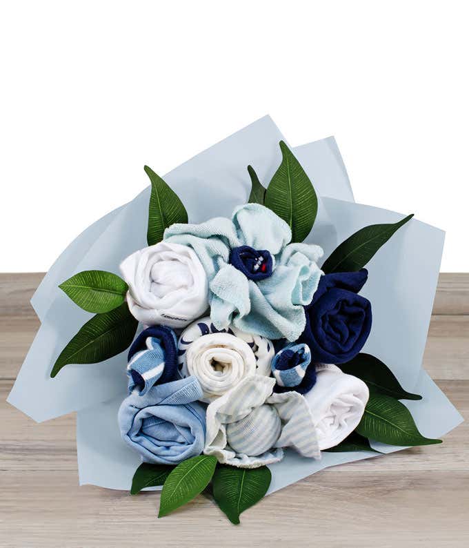 A blue flower bouquet made from rolled baby clothing items, including onesies, socks, and wash clothes, with green leaves wrapped in blue paper.