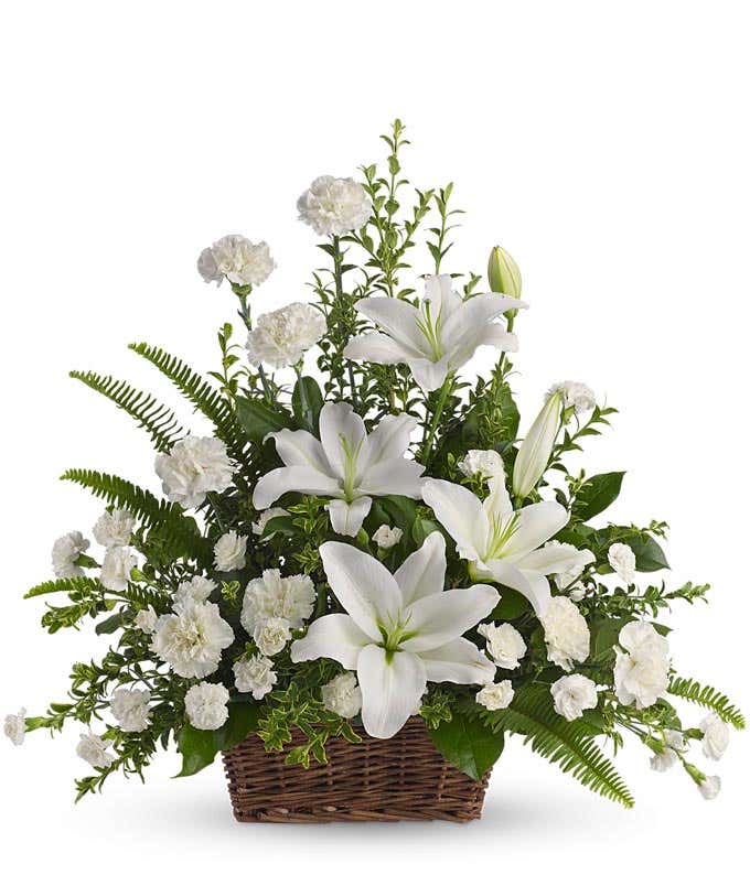 Funeral Arrangement: White Oriental Lilies, carnations, miniature carnations, and floral greenery in a brown wicker basket, symbolizing purity and remembrance.