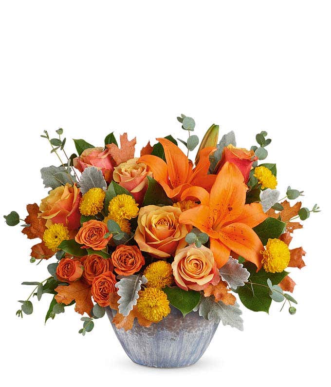 A bright and cheerful arrangement featuring orange roses, orange spray roses, orange lilies, and yellow cushion mums, all beautifully presented in a keepsake bowl.