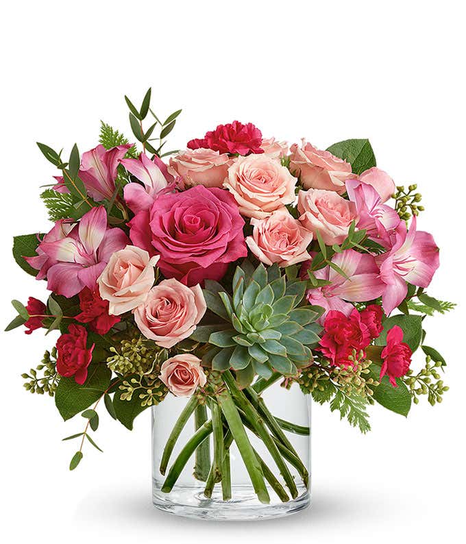 A vibrant floral arrangement featuring pink mini roses, pink alstroemeria, pink mini carnations, a succulent plant, and hot pink roses in deluxe and premium versions. This lush pink mix offers a charming and elegant display.