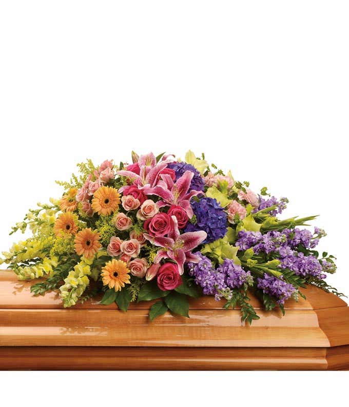 Vibrant casket spray featuring Purple Hydrangea, Hot Pink Roses, Peach Spray Roses, Pink Stargazer Lilies, Miniature Peach Gerberas, Green Gladioli, Pink Carnations, Yellow Snapdragon, and Floral Greenery, a colorful tribute to cherish.