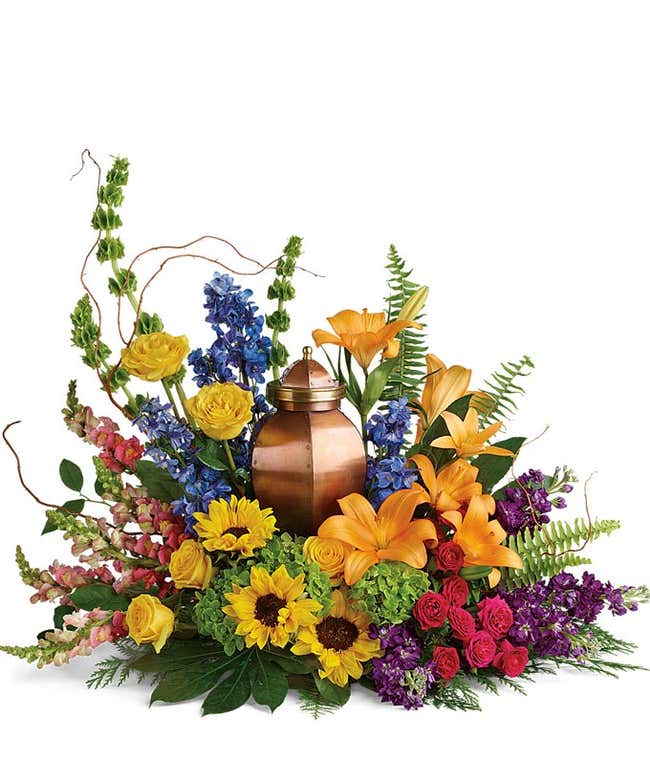 Funeral Cremation Adornment: Green hydrangea, yellow roses, hot pink spray roses, orange asiatic lilies, yellow sunflowers, bells of Ireland, blue delphinium, orange snapdragons, purple stock, and floral greenery, symbolizing remembrance and celebration o