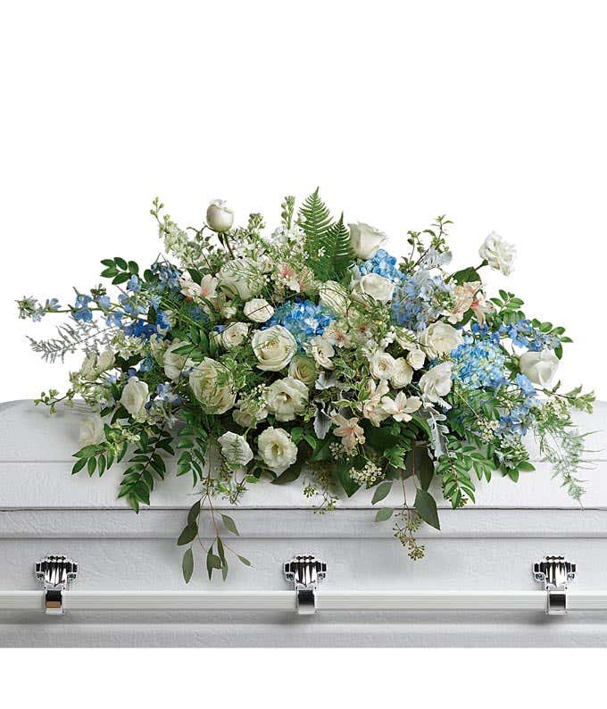 Funeral Casket Spray: Blue hydrangea, white roses, spray roses, alstroemeria, lisianthus, delphinium, larkspur, and stock flowers, accented with floral greenery, symbolizing serenity and remembrance.