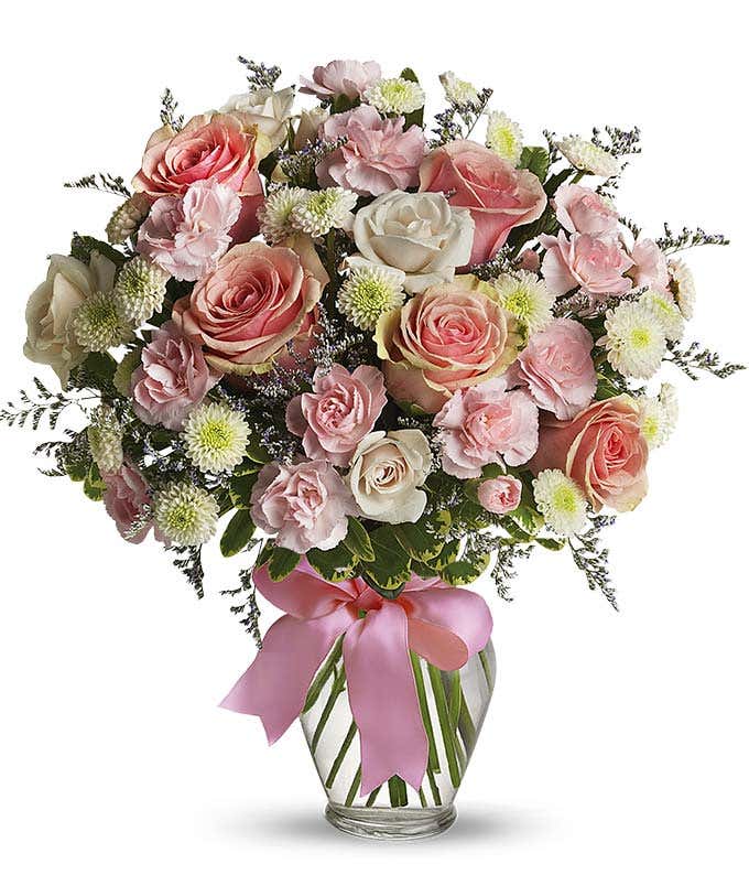 Floral arrangement featuring pink roses, white roses, mini carnations, and green poms in a clear glass vase with a bow.