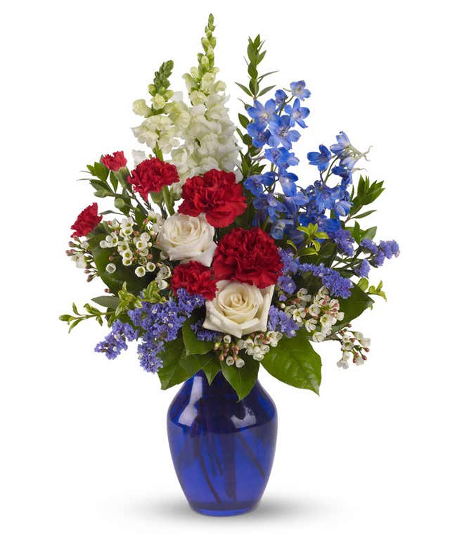 Patriotic floral arrangement with White Roses, Light Blue Delphinium, Red Carnations, Red Miniature Carnations, White Snapdragons, and Cobalt Blue Vase.