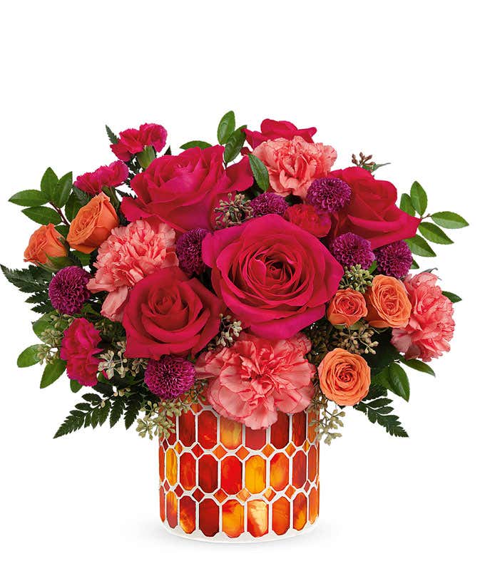 A vibrant floral arrangement featuring hot pink roses, orange spray roses, orange carnations, purple button spray chrysanthemums, hot pink miniature carnations, seeded eucalyptus, leatherleaf fern, and huckleberry, all beautifully presented in an orange m