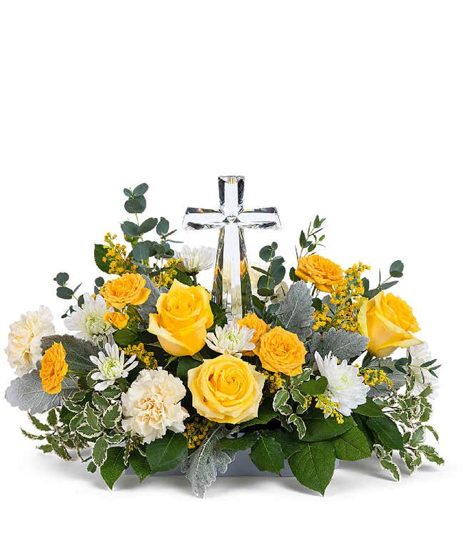 A stunning arrangement featuring yellow roses (deluxe &amp; premium only), yellow spray roses, light yellow carnations, white mums, yellow solidago, and floral greens, elegantly accented with a crystal cross. This vibrant mix offers a bright and uplifting dis