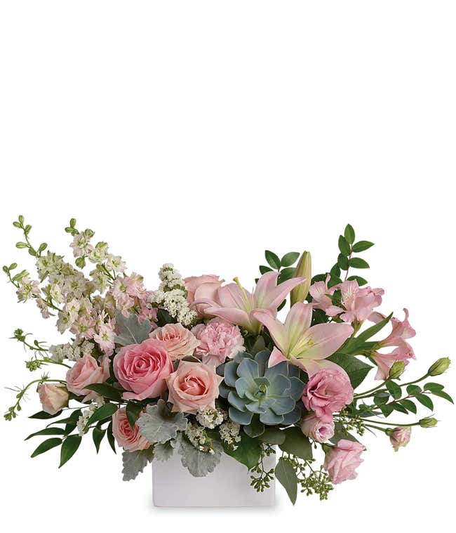 A beautiful arrangement featuring pink spray roses, pink lilies, pink alstroemeria, pink carnations, pink lisianthus, pink larkspur, white statice, and an echeveria succulent, all presented in a keepsake vase. This vibrant pink display offers a charming a