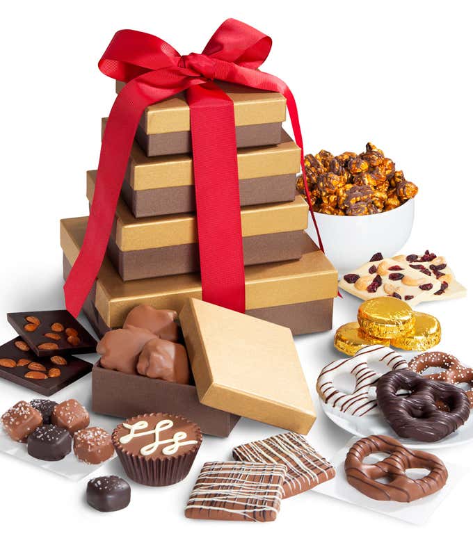 Gift tower with red ribbon filled with chocolate-covered pretzels, popcorn, nutty barks, pecan patties, graham crackers, peanut butter cup, sea salt caramels, and gold-wrapped sandwich cookies.