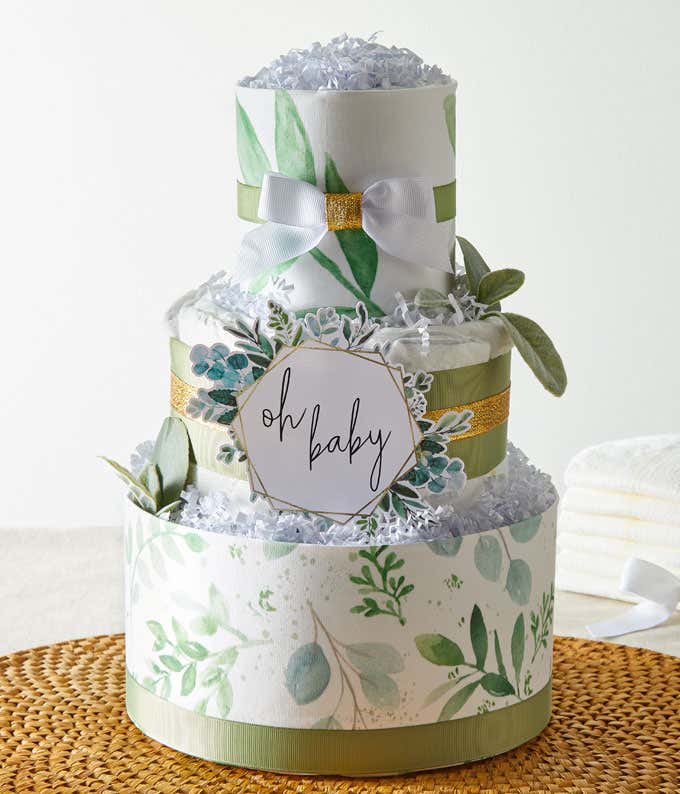 A three-tier diaper cake with green and white floral designs, topped with a white ribbon and 'Oh Baby' sign, surrounded by decorative greenery.