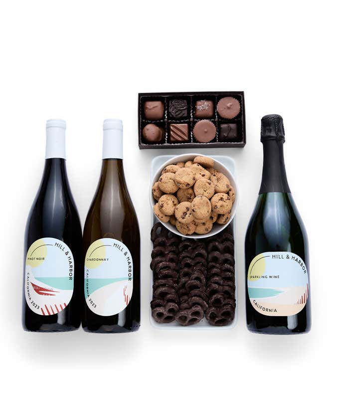 A gift set with three bottles of Hill & Harbor wine (Pinot Noir, Chardonnay, and sparkling wine), a box of assorted chocolates, chocolate-covered pretzels, and a box of mini chocolate chip cookies.